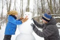 Little boy with his father building snowman in snowy park. Active outdoors leisure with children in winter. Kid during stroll in a Royalty Free Stock Photo