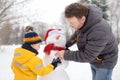 Little boy with his father building snowman in snowy park. Active outdoors leisure with children in winter Royalty Free Stock Photo