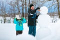 Little boy with his father making a snowman