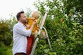 Little boy with his father picking apples in orchard. Child stands on a ladder and sniffs an apple