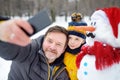 Little boy and his father taking selfie on background of snowman in snowy park. Active outdoors leisure with children in winter Royalty Free Stock Photo