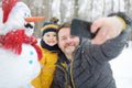 Little boy and his father taking selfie on background of snowman in snowy park. Active outdoors leisure with children in winter Royalty Free Stock Photo