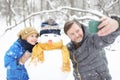 Little boy and his father taking selfie on background of snowman in snowy park. Active outdoors leisure with children in winter. Royalty Free Stock Photo