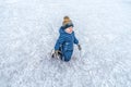 A little boy is on his knees, in winter, on a skating rink in winter overalls and a hat, he is smiling happily, first Royalty Free Stock Photo