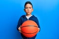 Little boy hispanic kid holding basketball ball skeptic and nervous, frowning upset because of problem
