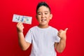 Little boy hispanic kid holding 100 dollars banknote smiling happy and positive, thumb up doing excellent and approval sign Royalty Free Stock Photo