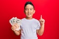 Little boy hispanic kid holding 10 united kingdom pounds banknotes smiling with an idea or question pointing finger with happy