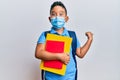 Little boy hispanic kid wearing medical mask going to school pointing thumb up to the side smiling happy with open mouth