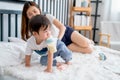 Little boy hold bottle of milk using mouth and crawl on bed with his mother take care on behide and they stay together in bedroom Royalty Free Stock Photo