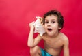 Little boy holding a big shell isolated on red background. concept of summer vacation, mobile phone, telephone operator Royalty Free Stock Photo