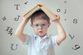 little boy holding a book above his head, letters fly out, dyslexia concept