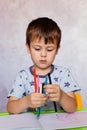 Little boy is holding color pencils. Boy, drawing a picture for fathers day. Small boy draws at the table