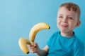 Little Boy Holding and eating an Banana on blue background, food, diet and healthy eating concept Royalty Free Stock Photo