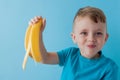 Little Boy Holding and eating an Banana on blue background, food, diet and healthy eating concept Royalty Free Stock Photo