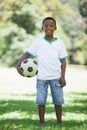 Little boy holding football in the park smiling at camera