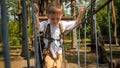 Little boy holding rope while crossing bridge strung between two trees in park. Active childhood, healthy lifestyle, kids playing Royalty Free Stock Photo