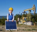 Little boy holding solar battery on the backdrop of oil rig.