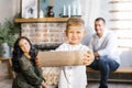 Little boy holds a log in his hands to light a fireplace against the background of happy parents. Cozy family winter Christmas Royalty Free Stock Photo