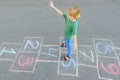 Little boy jumping by hopscotch drawn on asphalt. Child playing hopscotch game on playground on spring day. Top view Royalty Free Stock Photo