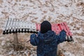 A little boy in a jumpsuit, hat and mittens plays a musical instrument in the winter in the park