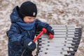 A little boy in a jumpsuit, hat and mittens plays a musical instrument in the winter in the park. The boy is having fun
