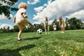 Little boy kicking the ball while parents and sister watching. Young family playing football on the grass field in the Royalty Free Stock Photo