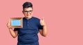 Little boy kid holding empty frame smiling happy and positive, thumb up doing excellent and approval sign Royalty Free Stock Photo