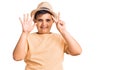 Little boy kid wearing summer hat and hawaiian swimsuit showing and pointing up with fingers number seven while smiling confident