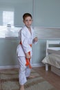 A little boy in a kimono with an orange belt stands in a fighting stance on a light background Royalty Free Stock Photo