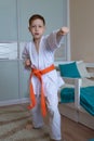 A little boy in a kimono with an orange belt stands in a fighting stance on a light background at home Royalty Free Stock Photo