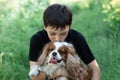 Little boy kissing friend dog Cavalier King Charles spaniel together in field meadow trees, greenery, street. Close up Royalty Free Stock Photo