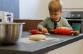 A little boy knead dough with a red rolling pin in the kitchen Royalty Free Stock Photo