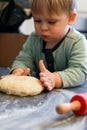 A little boy knead dough with a red rolling pin in the kitchen Royalty Free Stock Photo
