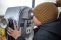 Little boy in a knitted hat looks through the observation coin binoculars at the autumn maple grove on the mountains in Vermont