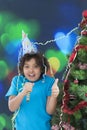 Little boy laughing on new year`s eve, wearing shiny hat and blowing horn,