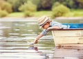 Little boy launch paper ship from old boat on the lake