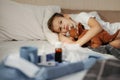 Little boy laying in bed with toy. Medicines and thermometer in foreground out of focus.