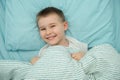 Little boy lays in his bed and smiles. Toddler in white shirt