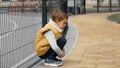 Little boy leaning on metal fence and sitting down. Child depression, problems with bullying, victim in school, emigration, Royalty Free Stock Photo
