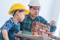 Little boy learning how to build brick wall from his construction father