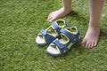 Little boy legs barefoot and sandals on the green artificial grass