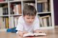 Little boy lies on his stomach and reading a book in the library. Royalty Free Stock Photo