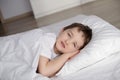 Little boy lies in white bed with eyes open