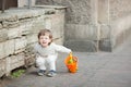 Little boy with long blond hair crying standing on the street. In his hand he is holding an orange bucket to play in the sandbox.