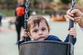 Little boy looking at camera while sitting in the swing at the playground in the park. Royalty Free Stock Photo