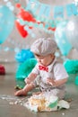 Little boy looking side with mouth covered in white icing and cake in decorated studio backdrop. Birthday cakesmash Royalty Free Stock Photo