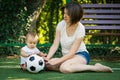 Little boy looking at soccer ball and exploring it sitting next to mother at football field. Toddler son playing with mom outdoors Royalty Free Stock Photo
