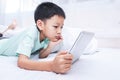 little boy looking at a tablet and playing games while lying on the bed at home. kid using smart devices online with his friends Royalty Free Stock Photo