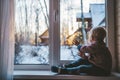 little boy looks out the window at home in winter waving his hand and feeling sad on a cold day Royalty Free Stock Photo
