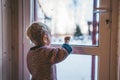 little boy looks out the window at home in winter waving his hand and feeling sad on a cold day Royalty Free Stock Photo